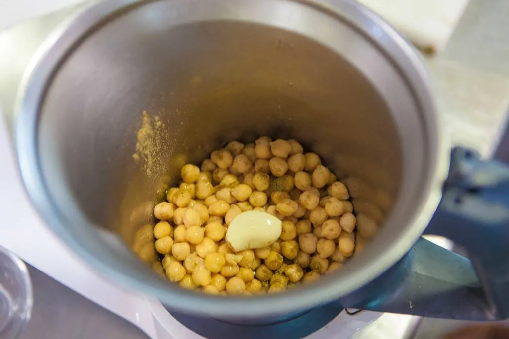 Mezclar los garbanzos, el ajo, el zumo de limón, un poco de comino y la sal y triturar con la batidora o la thermomix. Añadir poco a poco el aceite de oliva y el de sésamo, sin dejar de triturar, para que vaya emulsionando. Una vez conseguida la textura deseada, se reserva el hummus.