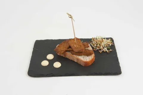 Porc tallat a tires, adobat amb espècies sobre una llesca de pa banyada amb maionesa al curri