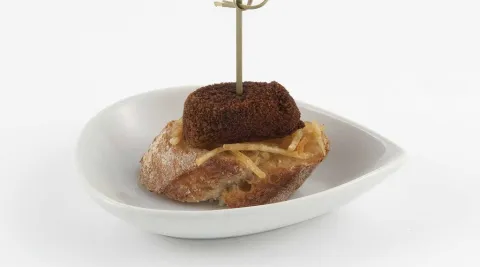 Croqueta de asado sobre cama de patatas paja y cebolla caramel·litzada