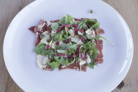Carpaccio de presa ibérica con rúcula, parmesano y vinagreta de frutos rojos